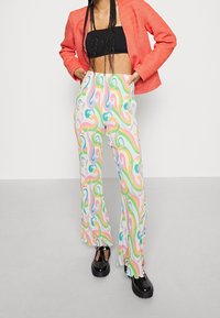 Pantalon large à motifs colorés, fabriqué dans un matériau léger, présentant des motifs tourbillonnants en rose, bleu et vert sur un fond blanc.