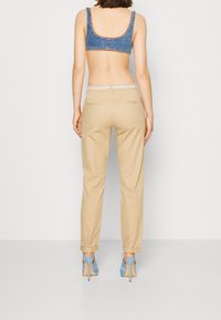 Bralette en denim à larges bretelles, associée à un pantalon beige fuselé avec une ceinture blanche à motifs et des ourlets retroussés, complétée par des talons bleus.