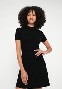 Μαύρο πλεκτό φόρεμα με στρογγυλή λαιμόκοψη και κοντά μανίκια, με υφασμένο μοτίβο "HUGO" σε κατακόρυφες γραμμές.