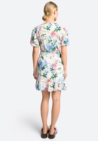 Bloemjurk van lichte stof met roze en blauwe patronen, korte puffmouwen, aansluitende taille en gerimpelde zoom. Gemaakt met casual schoeisel.