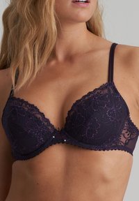 Paarse kanten beha met een ingewikkeld bloemenpatroon, gevoerde cups, verstelbare bandjes en decoratieve accenten in het midden. Zachte textuur en delicate uitvoering.
