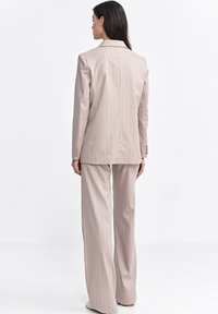 Jasnoróżowy garnitur w paski składający się z dopasowanej marynarki z klapami oraz szerokich spodni, wykonany z gładkiego materiału.