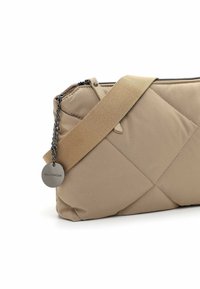 Borsa a tracolla beige trapuntata con una texture liscia, dotata di una ampia tracolla beige e un dettaglio in catena argentata con un'etichetta del marchio.