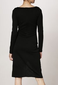 Černé šaty s dlouhými rukávy a těsným střihem, s kruhovým výstřihem a detailem na zip na zadní straně. Hladká textura, délka po kolena, decentní tvarování.