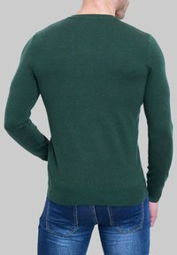 Pull vert à col rond avec des manches longues, fabriqué en tissu doux. Design ajusté, poignets et ourlet côtelés, porté avec un jeans bleu.