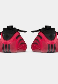 Coppia di scarpe sportive rosse e nere viste da dietro, con suole testurizzate e chiusure con lacci su sfondo bianco.