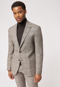 Grau karierter Anzug mit taillierter Passform, ausgestattet mit einem einreihigen Knopfverschluss, Reverskragen und einem schwarzen Rollkragenpullover darunter.