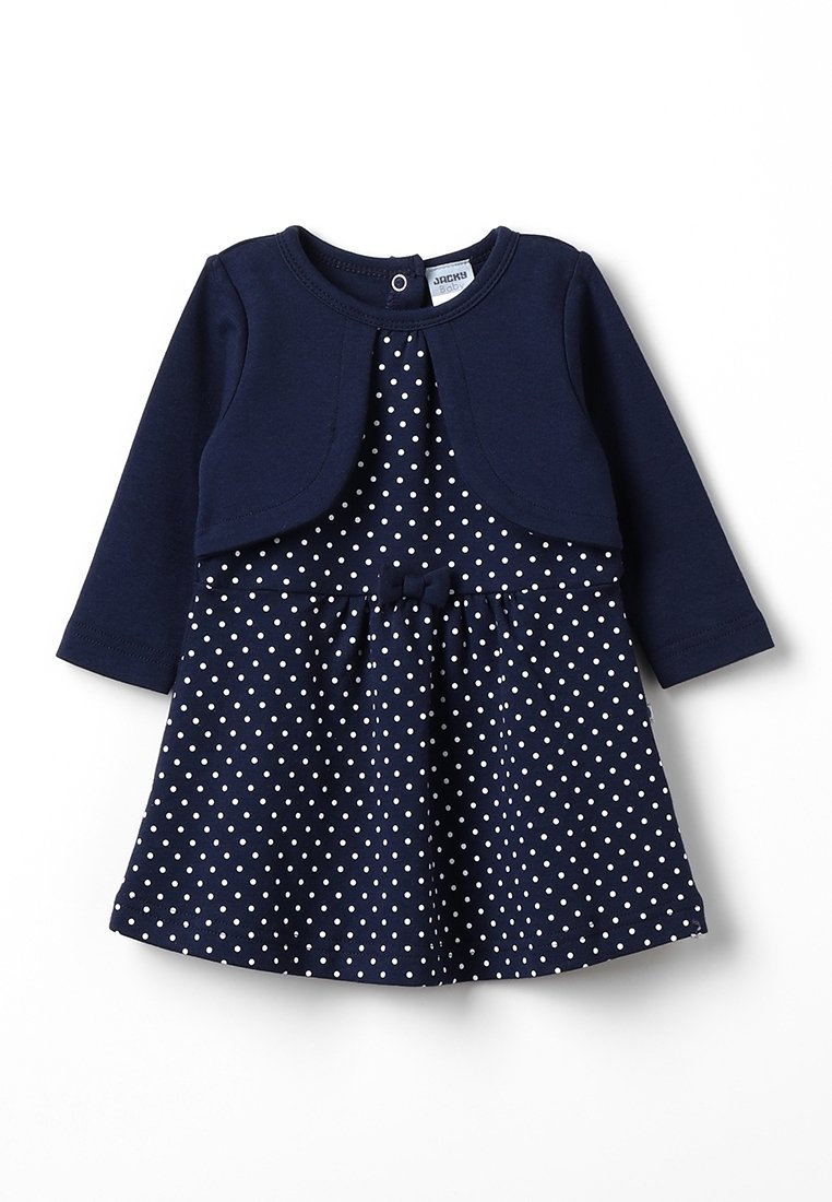 Robe bleu marine à pois blancs, à manches longues, accompagnée d'une veste courte assortie. Elle présente un nœud à la taille et un décolleté rond.