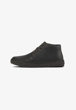Black leather ankle boots with a rounded toe and textured rubber sole, featuring minimal lacing on the front.