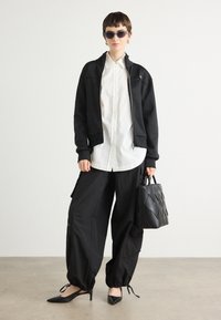 Black zip-up jacket, white button-up shirt, black cargo pants with drawstring hems, black pointed flats, and a textured black shoulder bag.
