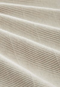 Beige geripptes Gewebe mit weicher Textur, das subtile erhabene Linien aufweist, die ein Wellenmuster über die Oberfläche des Materials bilden.