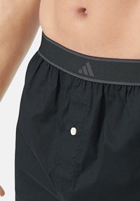 Černé bavlněné plavky s širokým elastickým pasem, který má šedé akcenty a bílé knoflíkové detaily, navržené pro pohodlí a dokonalý střih.