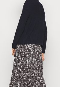 Granatowy sweter dzianinowy o luźnym kroju, zestawiony z czarną i kremową spódnicą w kwiatowy wzór, z delikatnymi akcentami kwiatowymi i plisowanym designem.