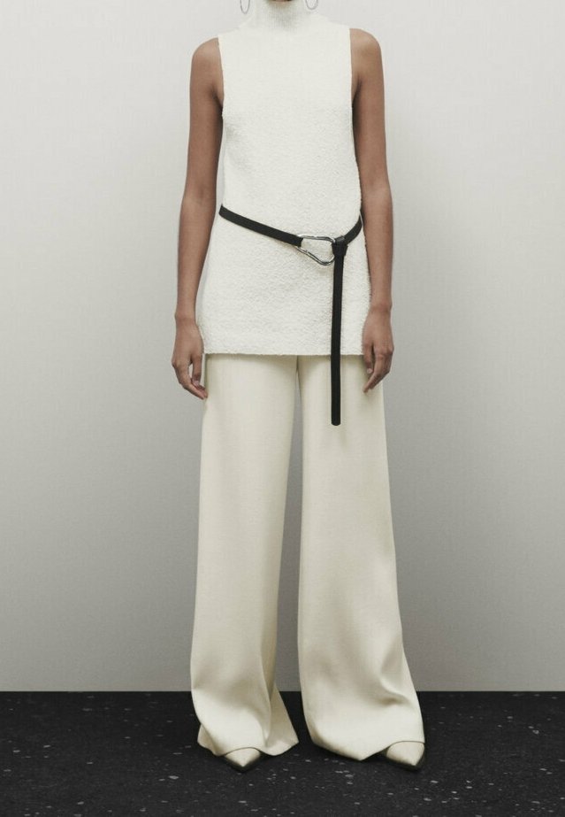 Tunique sans manches beige texturée avec une ceinture noire, associée à un pantalon large crème. Design minimaliste et finition en tissu lisse.