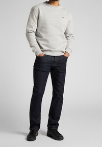 Szary polarowy sweatshirt z okrągłym dekoltem i małym logo, w połączeniu z ciemnoniebieskimi dżinsami i czarnymi sneakerami. Luźny zestaw ubrań.