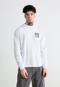 White long-sleeve shirt with a rectangular black "OBEY" logo on the left chest. The fabric appears soft, with a crew neck design.