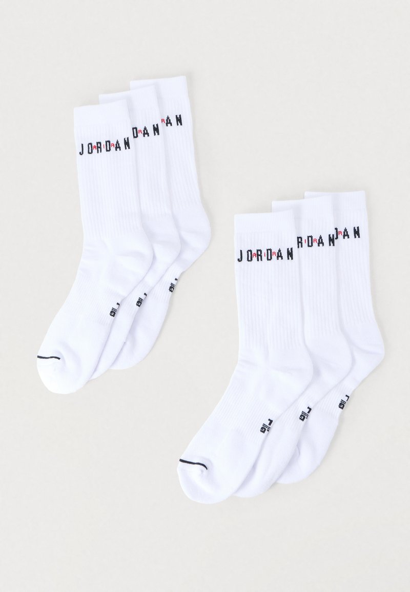Σετ λευκές βαμβακερές κάλτσες με ριμπ υφή και μαύρα γράμματα που σχηματίζουν τη λέξη "JORDAN" με κόκκινες λεπτομέρειες. Εμφανίζονται τέσσερα ζευγάρια, μεσαίου μήκους.