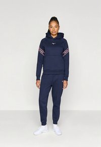 Σετ μπορντό φούτερ με κουκούλα και παντελόνι φόρμας από βουρτσισμένο ύφασμα. Το φούτερ διαθέτει τσέπη καγκουρό και ροζ λογότυπα στα μανίκια.