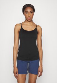 Svart ärmlös linne med tunna axelband, tillverkat av slät tyg. I kombination med blå shorts med synlig sömnad och sidofickor.