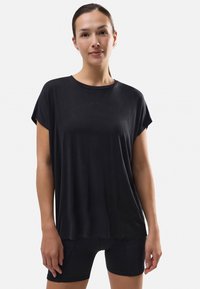 Top negro de manga corta con cuello redondo y corte holgado. Fabricado en una tela suave, presenta un sutil detalle de costura en forma de V en el frente.