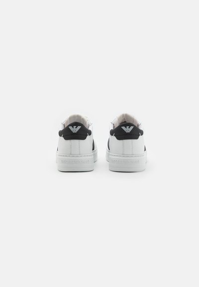 Vita låga sneakers med en svart bakheel och präglad logotyp. Slätt material med en enkel design. Rena linjer och minimala accenter.