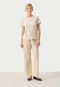 T-shirt beige a maniche corte abbinato a pantaloni larghi beige chiaro. L'outfit presenta una texture liscia e un design semplice e minimalista.
