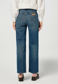 Vaqueros rectos de color azul oscuro con cintura alta, que cuentan con una etiqueta tejida en el bolsillo trasero y un ligero desgastado para añadir textura.