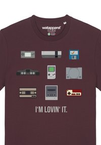 T-shirt bordeaux présentant huit consoles de jeux rétro et un graphisme de manette, avec le texte "J'ADORE" en blanc en dessous.