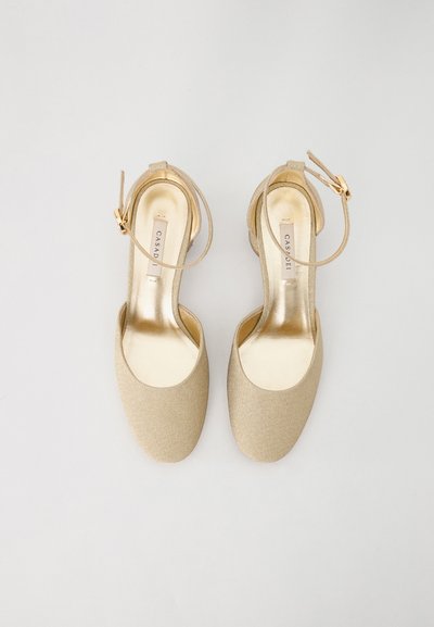 Goldene Glitzer-Ankle-Strap-Schuhe mit runden Zehen. Glattes Innenfutter und strukturierte Außenseite. Verfügt über einen schlanken Absatz und einen verstellbaren Knöchelriemen.