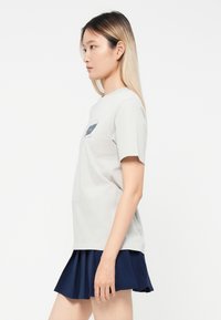 Tricou din bumbac gri deschis, cu mâneci scurte și guler rotund, având un design grafic bleumarin pe piept, asociat cu o fustă plisată bleumarin.