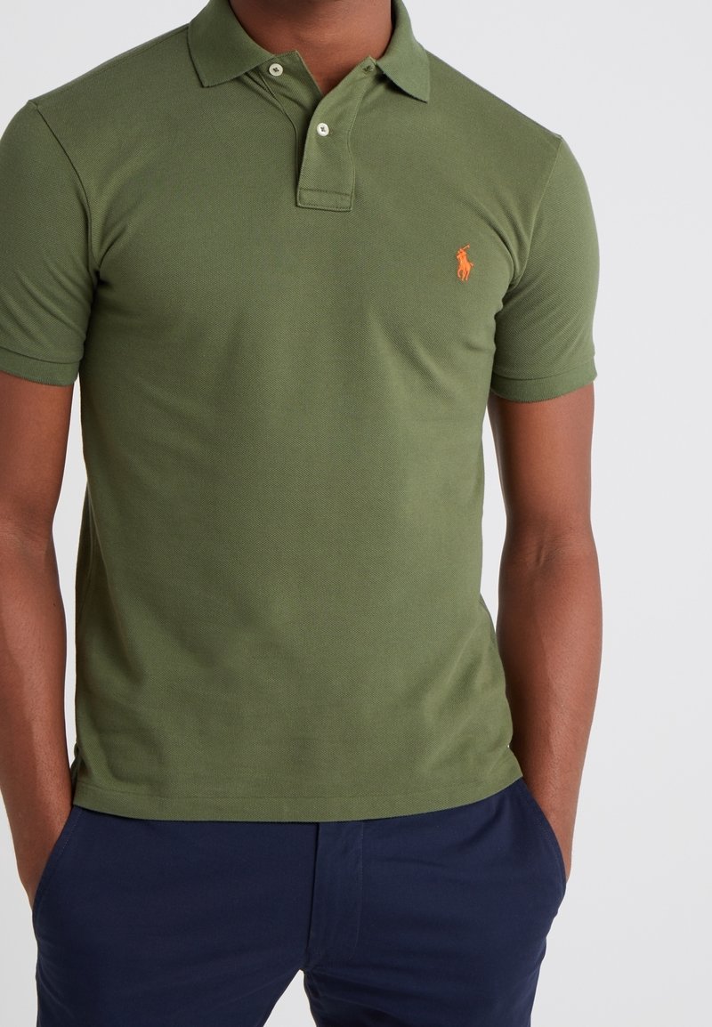 Polo tričko olivové barvy z pevného bavlněného materiálu, s klasickým límečkem a třemi knoflíky, s oranžovým logem na levé části hrudi.