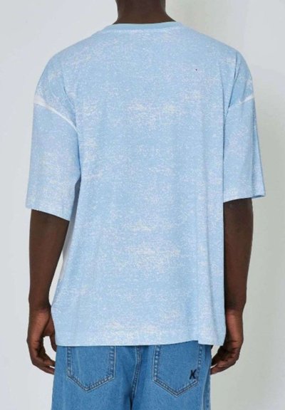 T-shirt di cotone azzurro chiaro con una texture morbida, caratterizzata da una vestibilità rilassata e maniche corte, vista da dietro. Dettagli bianchi sottili nel design.