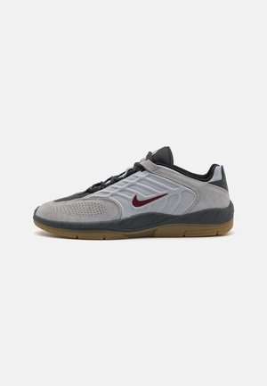 Nike obutev z zgornjim delom iz sivega semiša in mrežaste tkanine, črnimi vezalkami, rdečim logotipom in gumijastim podplatom. Nizka oblika.