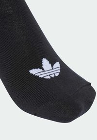 Čierna ponožka s rebrovanou textúrou, s bielym logom Adidas trefoil a tromi horizontálnymi pruhmi na hornej časti.