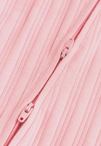 Närbild av en dubbel rosa dragkedja på ett räfflat rosa tyg, delvis stängd och vertikalt justerad.