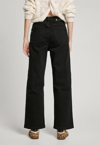 Svarta vida jeans gjorda av denim, med bakfickor och hög midja. Matchade med mönstrade skor och en texturerad tröja.