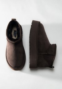 Bruine suède enkellaarsjes met een gestructureerd oppervlak, gevoerd met imitatiebont en een stevige rubberen zool. Voorzien van een lus aan de achterkant voor gemakkelijk aantrekken.