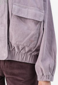 Lavendel corduroy jack met elastische tailleband en manchetten, met een klepzak en een kleine geborduurde hartdetail nabij de zoom.