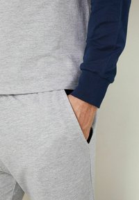 Outfit sportivo da uomo composto da una maglietta grigia chiaro a maniche corte e maniche lunghe blu navy, progettato con una vestibilità comoda e tasche laterali.