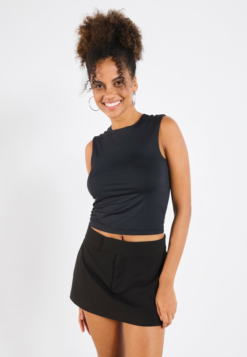 Black sleeveless cropped top with a smooth texture, paired with a black mini skirt featuring a simple design and front pockets.
