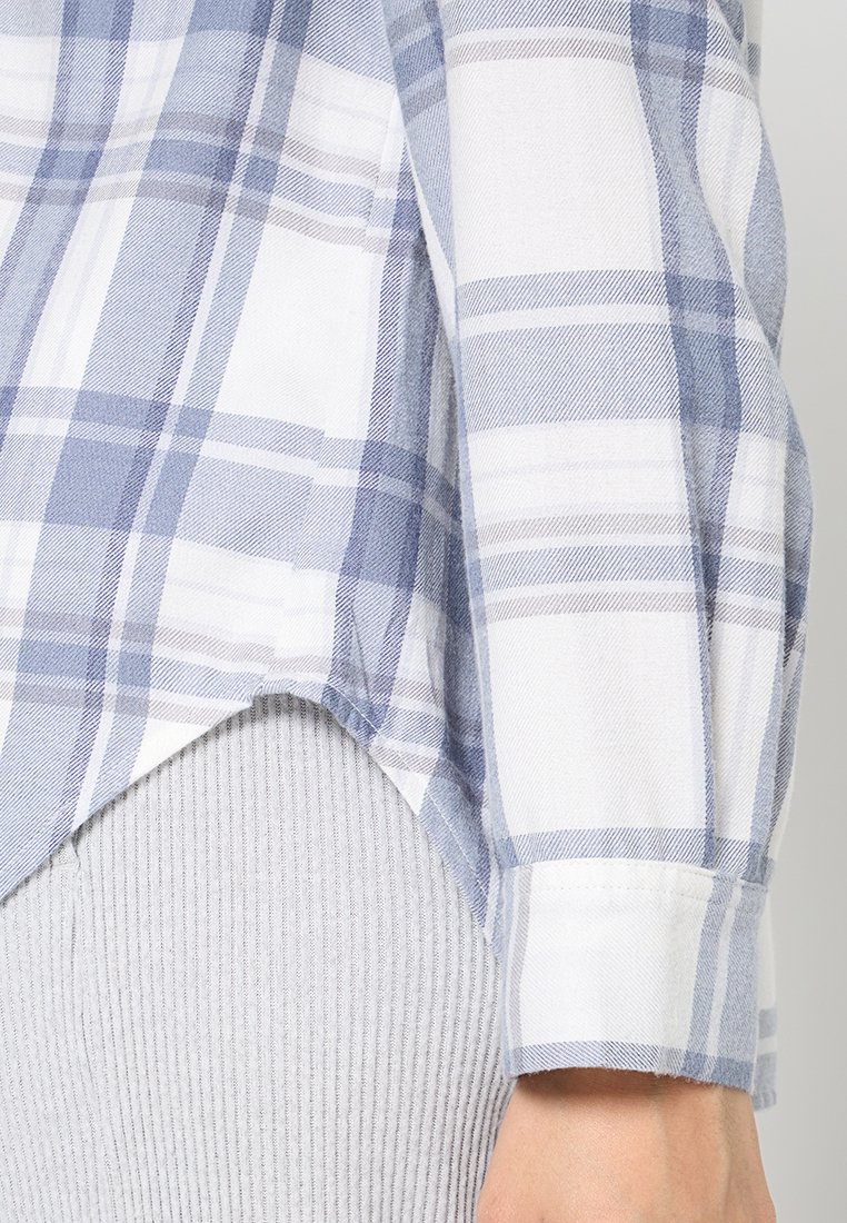 Blau-weiß kariertes Hemd aus weicher Baumwolle, mit abgerundetem Saum und hochgerollten Ärmeln. Darunter strukturiertes graues Rippgewebe.
