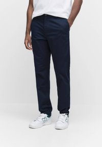 Marineblaue Chinos aus Baumwolle mit glatter Textur. Verfügen über einen geraden Beinschnitt, seitliche Taschen und einen Metallknopfverschluss.
