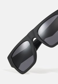 Mustad prillid matte raami ja suurte ruudukujuliste läätsedega, tumedate hallide toonidega. Omavad sujuvat tekstuuri ja minimalistlikku disaini.