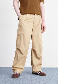 Beige cargo bukser med en afslappet pasform, med sidelommer, en elastisk talje og matchende brune sko med hvide striber.