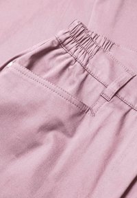 Roze stof met een gladde textuur heeft een elastische taille, zakken en gestikte details, wat de casual broekontwerp benadrukt.