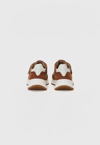 Brown suede sneakers with a white rubber sole, featuring a smooth texture and a zigzag design on the heel accent. Zipper detail at the back.