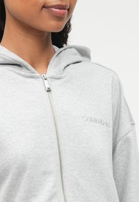 Γκρίζα φούτερ με κουκούλα, διαθέτει ασημί φερμουάρ και κεντητό λογότυπο "Calvin Klein". Μαλακό υλικό με άνετη εφαρμογή.