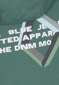 Zielona bawełniana bluza z dużym białym graficznym napisem oraz geometrycznymi kształtami w odcieniach niebieskiego, szarego i zielonego.