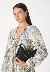 Μαύρη δερμάτινη τσάντα με υφή, με ασημένιο αλυσίδα και ρυθμιζόμενο λουρί. Το μοντέλο φοράει ένα φόρεμα μακρυμάνικο με ανθισμένο σχέδιο.