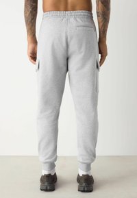 Graue Sweatpants mit einem Kordelzugbund, eng zulaufendem Schnitt, seitlichen Cargo-Taschen und gerippten Bündchen. Der Stoff wirkt weich und strukturiert, ideal für Komfort.